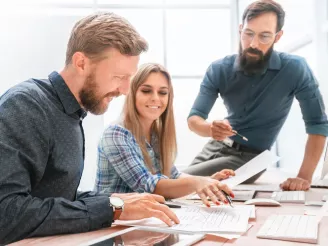 Three colleagues discussing printed documents at desk