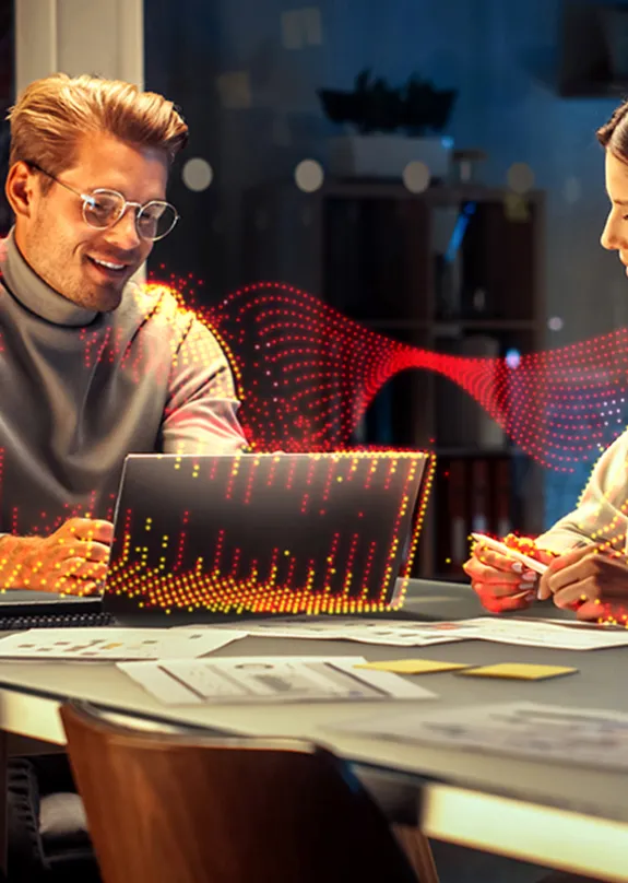 Man and a Woman sat a table, both looking at a laptop whilst talking 